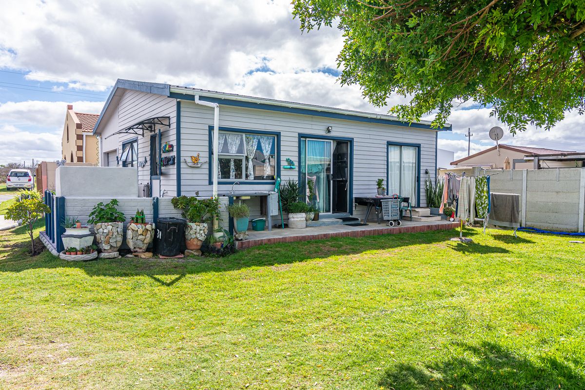 Rear view of a single-story house featuring weatherboard cladding, a paved patio area, and a private garden with a concrete boundary wall.