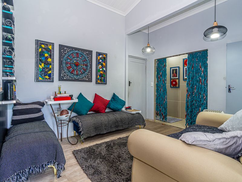 A living room area featuring tiled flooring, vaulted ceilings, and pendant lighting, providing a functional space with direct access to an adjacent room.