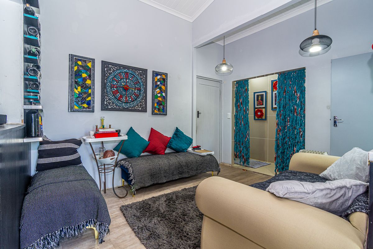 A living room area featuring tiled flooring, vaulted ceilings, and pendant lighting, providing a functional space with direct access to an adjacent room.