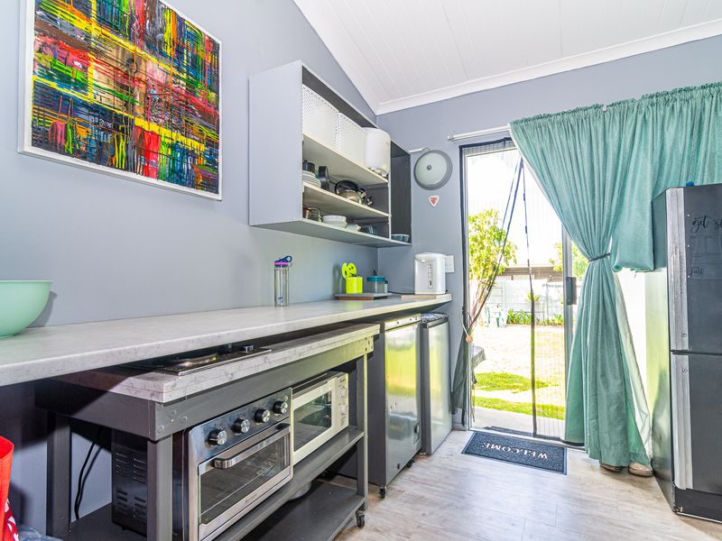 A functional scullery or utility area featuring built-in shelving, laminate flooring, and direct access to the rear garden through a sliding glass door.