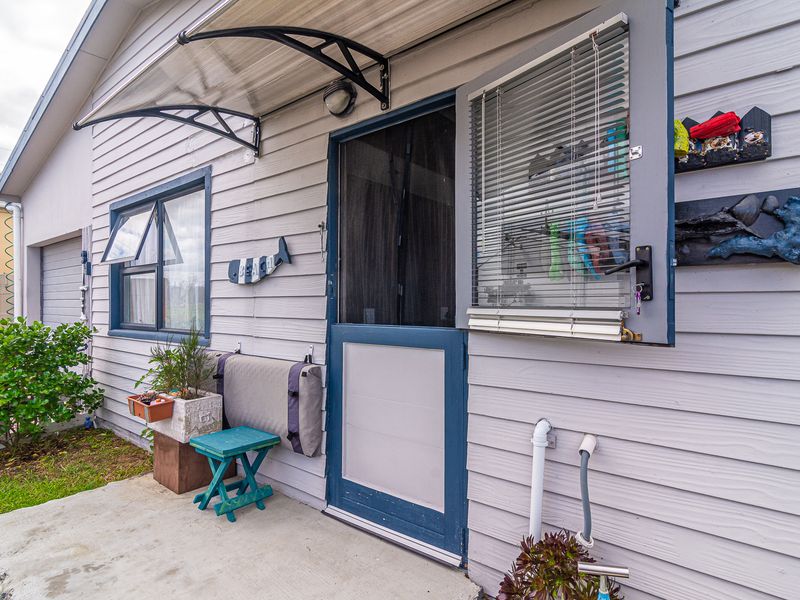 Front entrance area featuring weatherboard cladding, a protective awning over the door, and a security screen door with integrated window blinds.