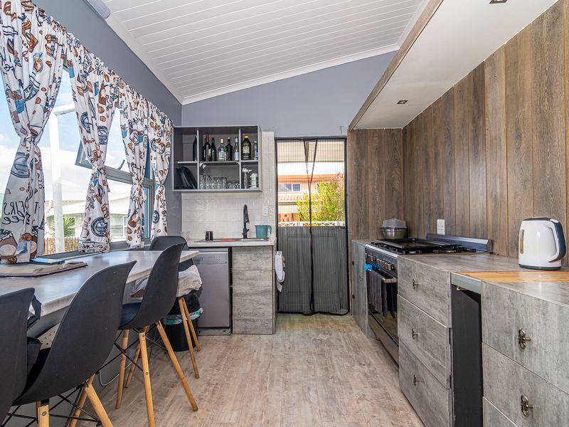 A compact kitchen featuring modern grey cabinetry, timber-look wall paneling, a freestanding oven, and a breakfast bar area with large windows.
