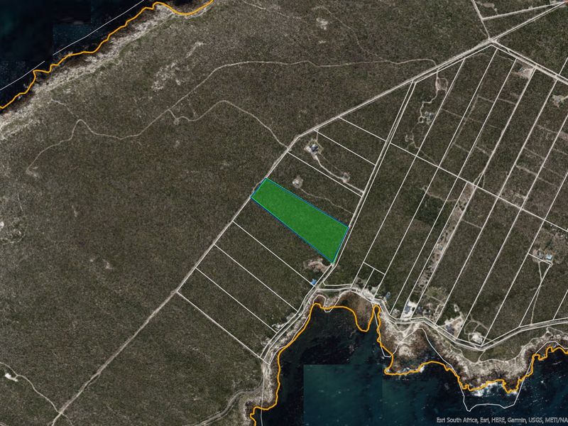 Aerial view of a vacant residential land parcel highlighted in green, situated in a coastal area with surrounding natural vegetation.