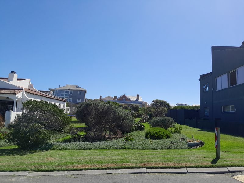 A view of a residential vacant plot featuring established garden landscaping and lawn, situated between existing neighboring properties.