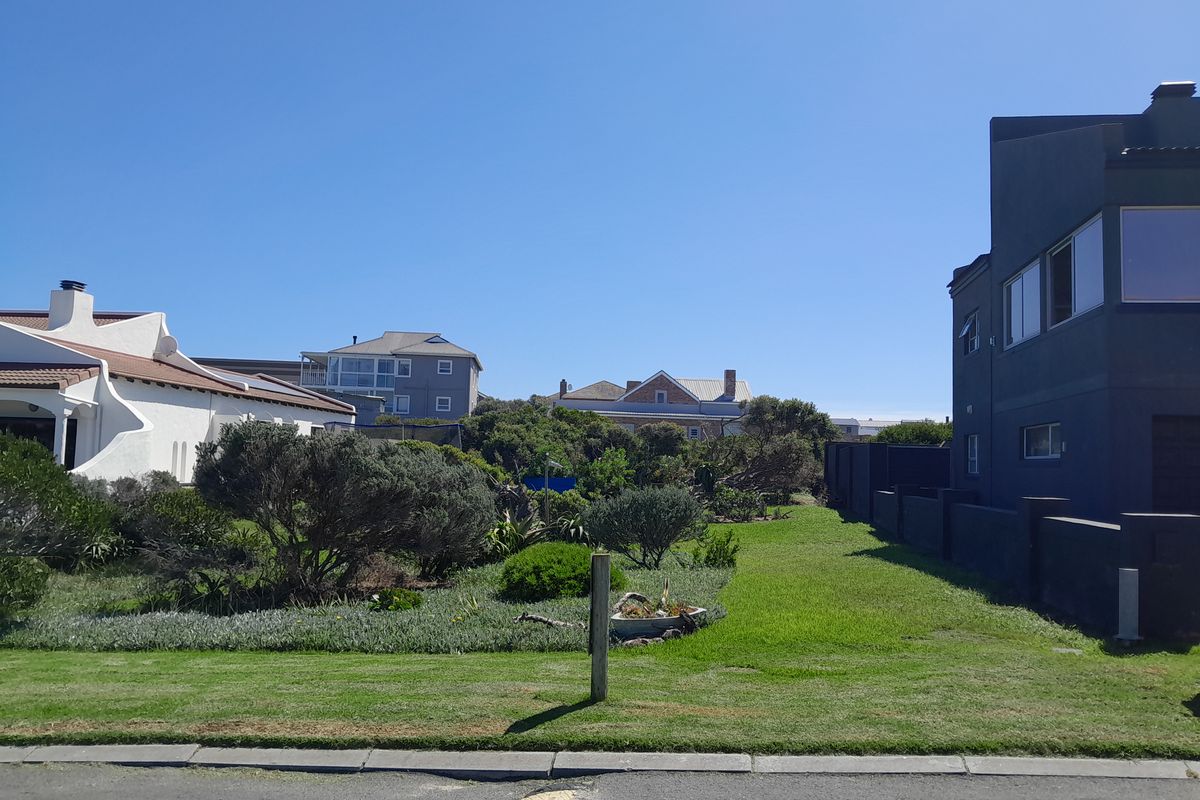A view of a residential vacant land plot featuring a well-maintained lawn and established garden borders, situated between existing neighboring properties.