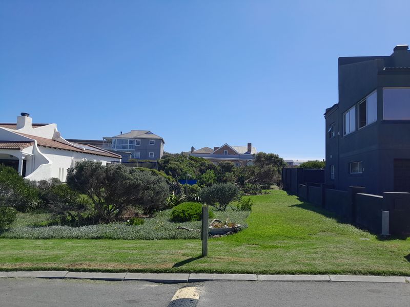 A view of a residential vacant land plot featuring a well-maintained lawn and established garden borders, situated between existing neighboring properties.