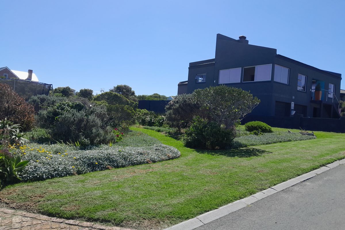 A well-maintained front garden with lush lawn and established landscaping, adjacent to a paved driveway and street view of the property.