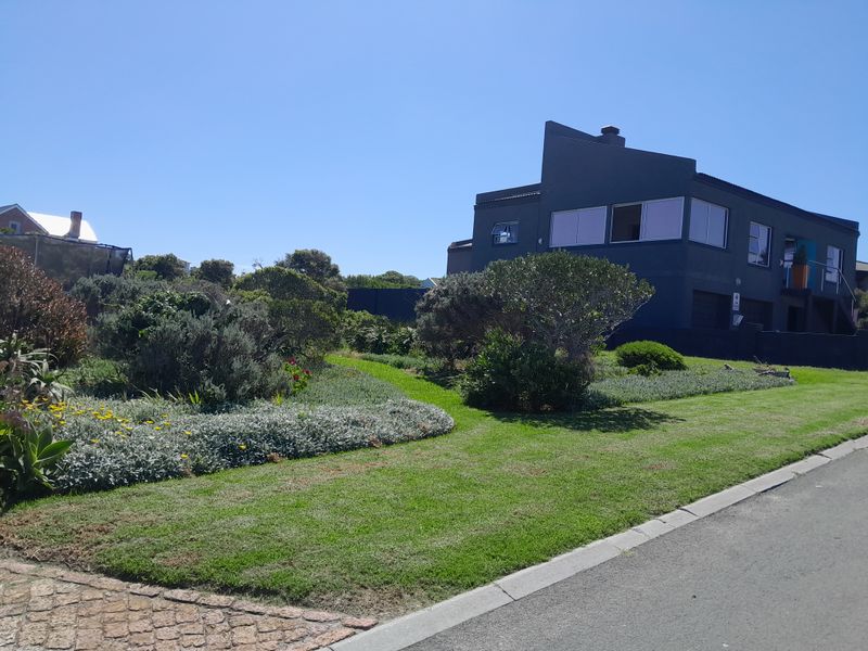 A well-maintained front garden with lush lawn and established landscaping, adjacent to a paved driveway and street view of the property.
