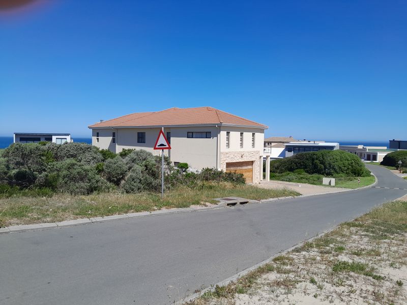 A view of a residential property from the street, featuring a tiled roof, garage, and paved driveway in a coastal setting.