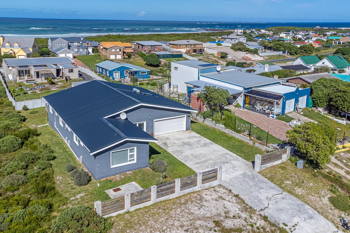 Aerial view of a coastal residential property featuring a metal roof, concrete driveway, and secure boundary fencing in a beachside neighbourhood.