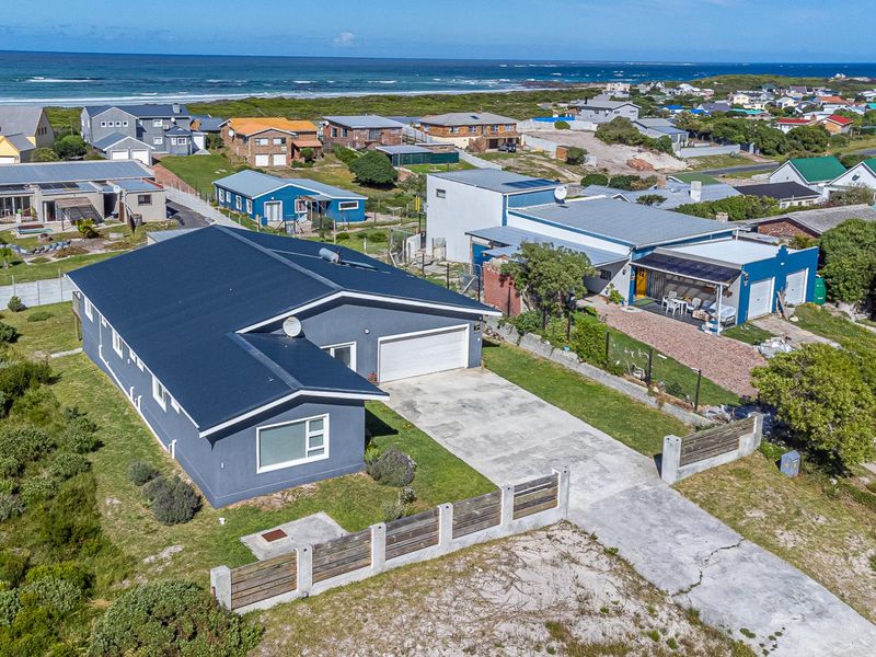 Aerial view of a coastal residential property featuring a metal roof, concrete driveway, and secure boundary fencing in a beachside neighbourhood.