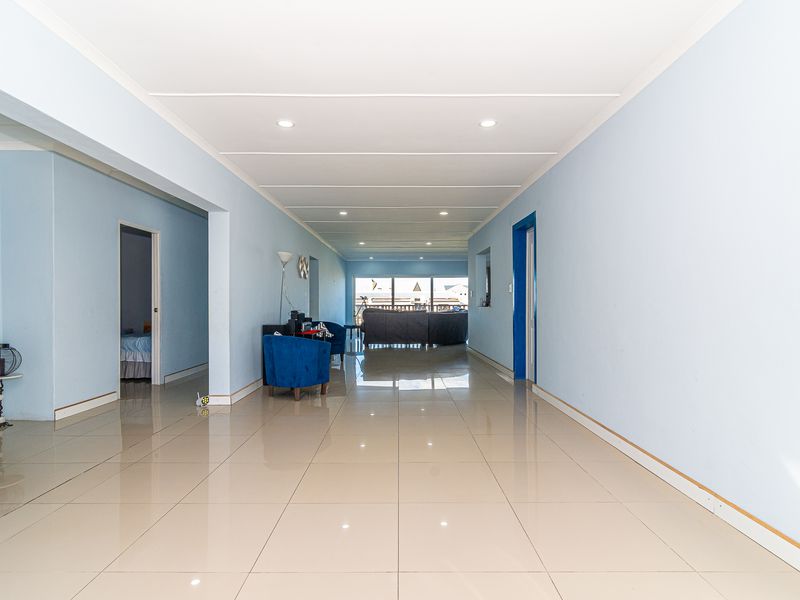 Spacious open-plan living area featuring neutral tiled flooring, recessed downlighting, and a bright, airy layout leading toward a rear view.