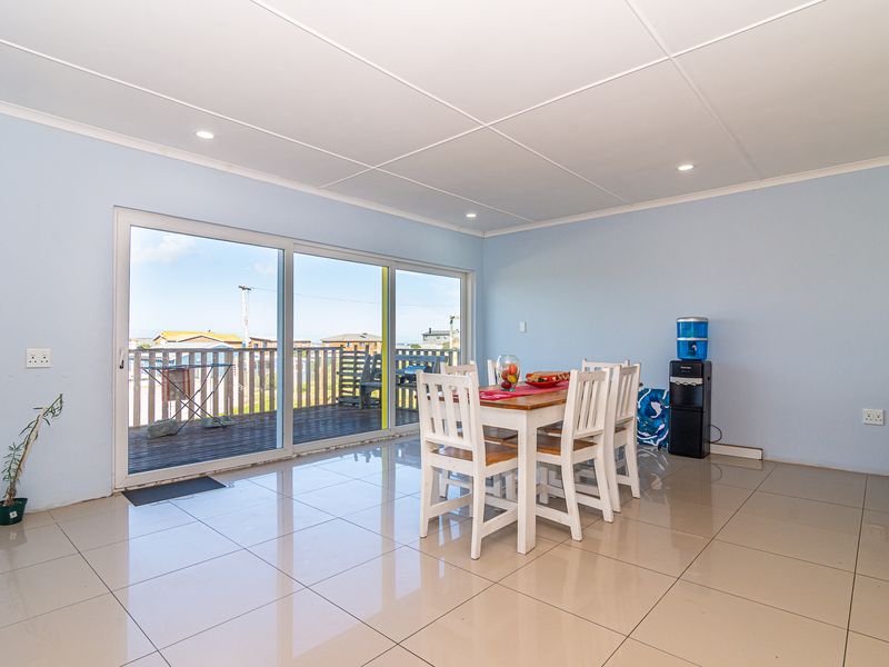 Open plan living and dining area featuring large sliding glass doors leading to an outdoor deck, with neutral tiled flooring and recessed lighting.