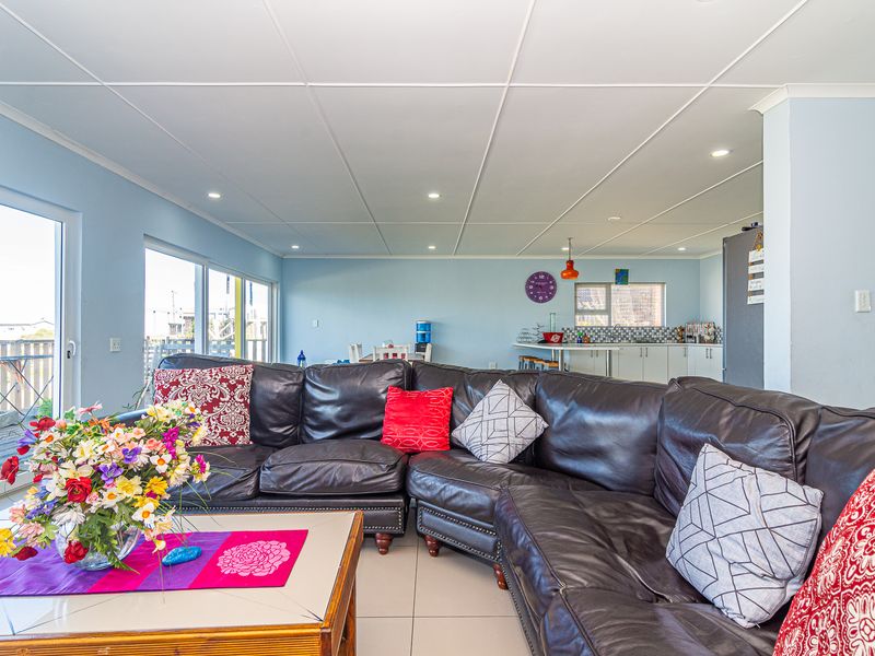 Spacious open-plan living area featuring tiled floors, recessed lighting, and direct access to an outdoor deck, seamlessly connecting to a functional kitchen space.