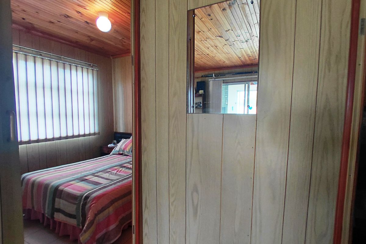 A bedroom featuring dated timber wall paneling and a matching timber ceiling, with vertical blinds and a simple flush mount light fixture.