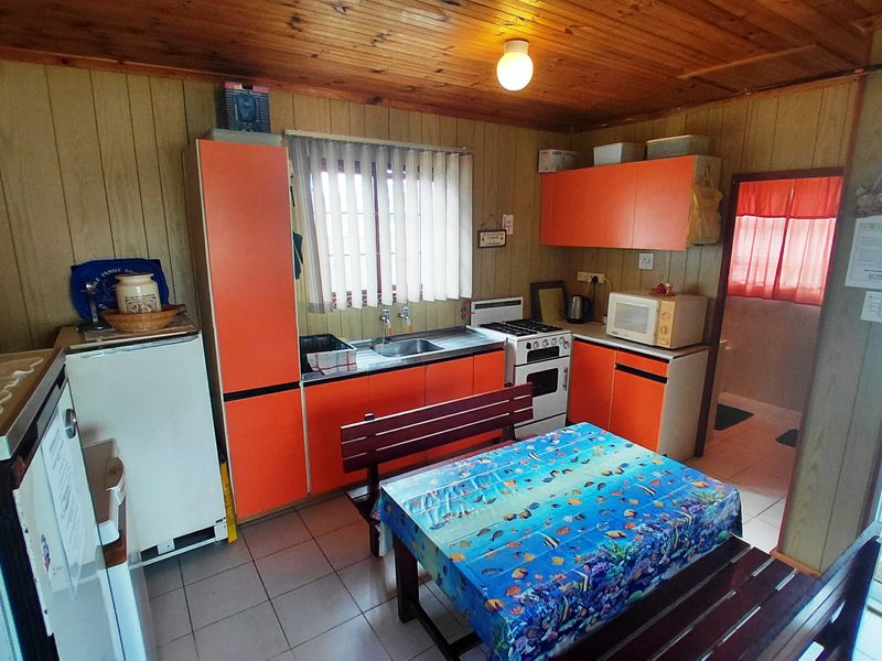 A dated kitchen featuring orange cabinetry, timber wall paneling, a stainless steel sink, and a freestanding stove with tiled flooring.