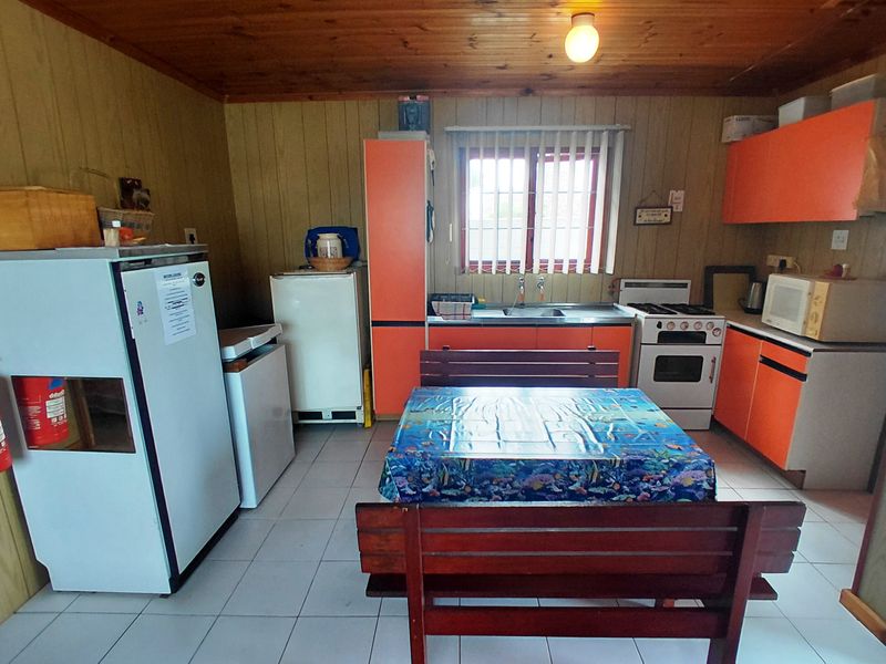 A dated kitchen featuring orange cabinetry, timber ceiling paneling, tiled floors, and a functional layout with a stainless steel sink and freestanding oven.
