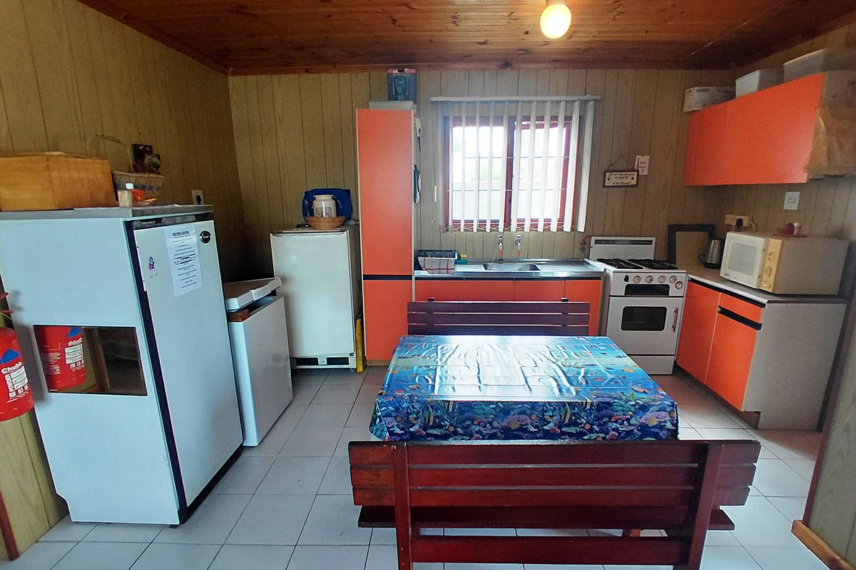 A dated kitchen featuring orange cabinetry, timber ceiling paneling, tiled floors, and a functional layout with a stainless steel sink and freestanding oven.