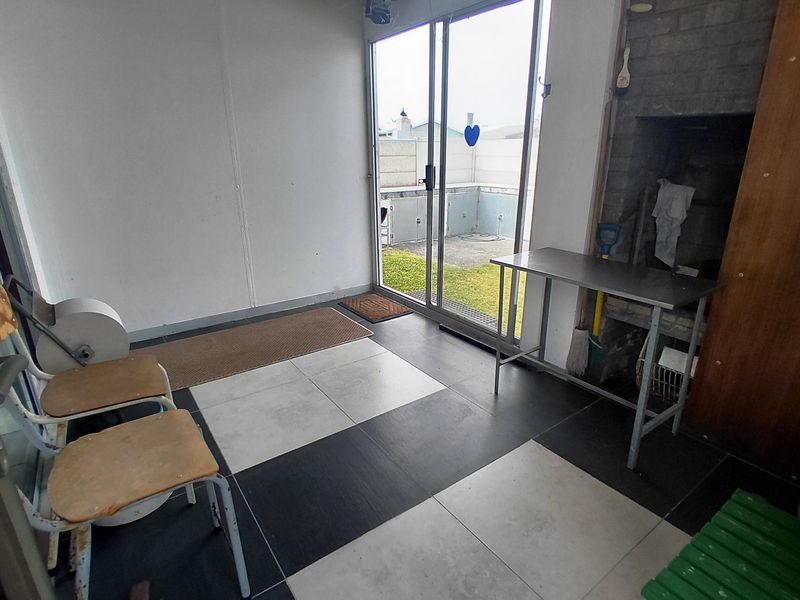 Covered patio area featuring a built-in braai, tiled flooring, and sliding glass doors providing direct access to the rear garden.