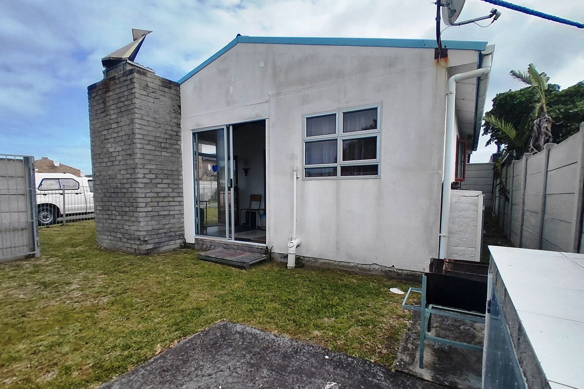 Rear exterior view of the property featuring a brick chimney, sliding glass door access, and a concrete patio area within a fenced yard.