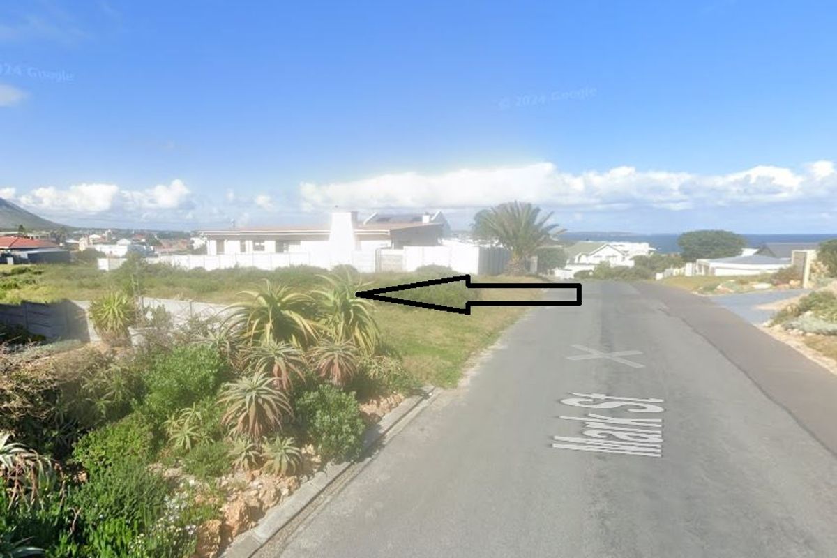 Street view of a vacant residential plot featuring established landscaping and boundary walling in a coastal neighborhood.