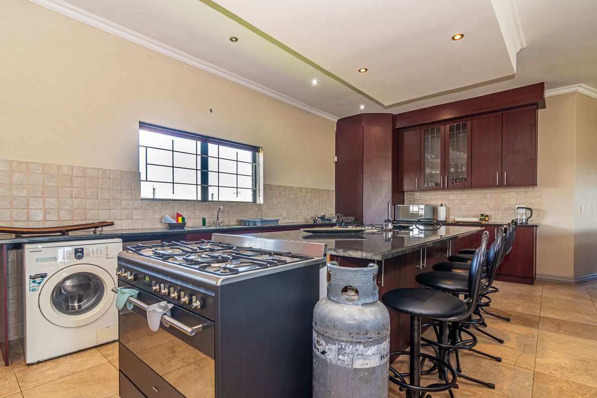 Spacious kitchen featuring dark wood cabinetry, granite countertops, a gas stove, and integrated laundry facilities with tiled flooring and recessed lighting.