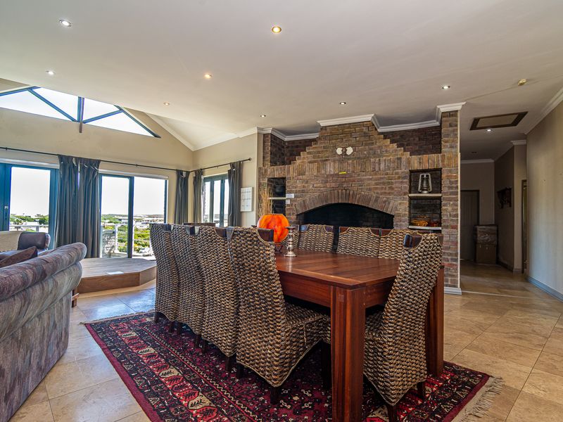 Spacious open-plan living and dining area featuring a prominent brick fireplace, vaulted ceilings, tiled floors, and large sliding doors leading to an outdoor space.