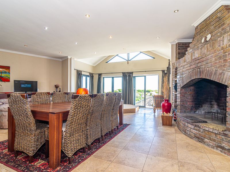 Spacious open-plan living and dining area featuring a prominent brick fireplace, vaulted ceilings, and large glass doors leading to an outdoor space.