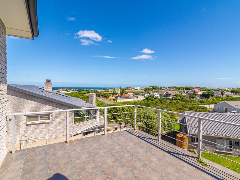 An elevated balcony with tiled flooring and metal railings, offering expansive views of the surrounding neighborhood and distant coastline.
