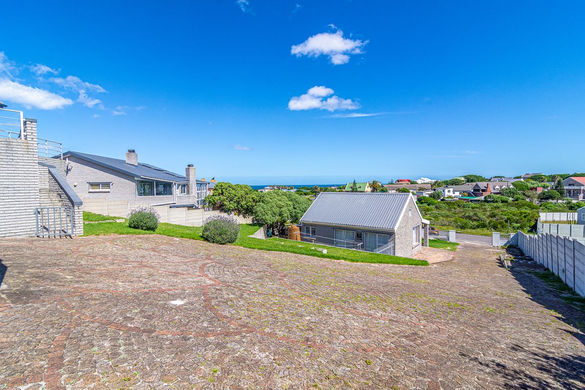 A wide-angle view of the rear exterior featuring a large cobblestone driveway, brick building structures, and a clear view of the surrounding coastal landscape.