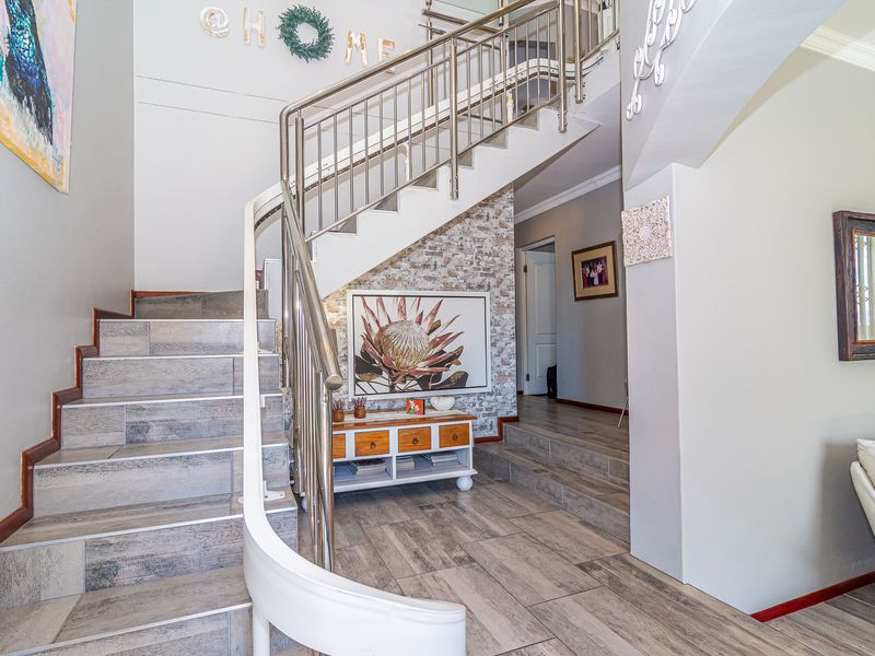 Welcoming entrance hall featuring a modern staircase with stainless steel balustrades and stylish wood-look tiled flooring.