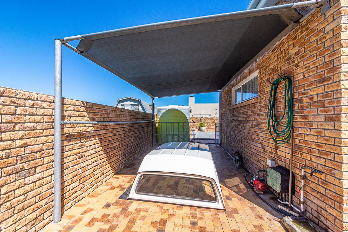 A paved side yard area featuring face brick walls, a shade cloth canopy, and integrated water storage and pumping infrastructure.