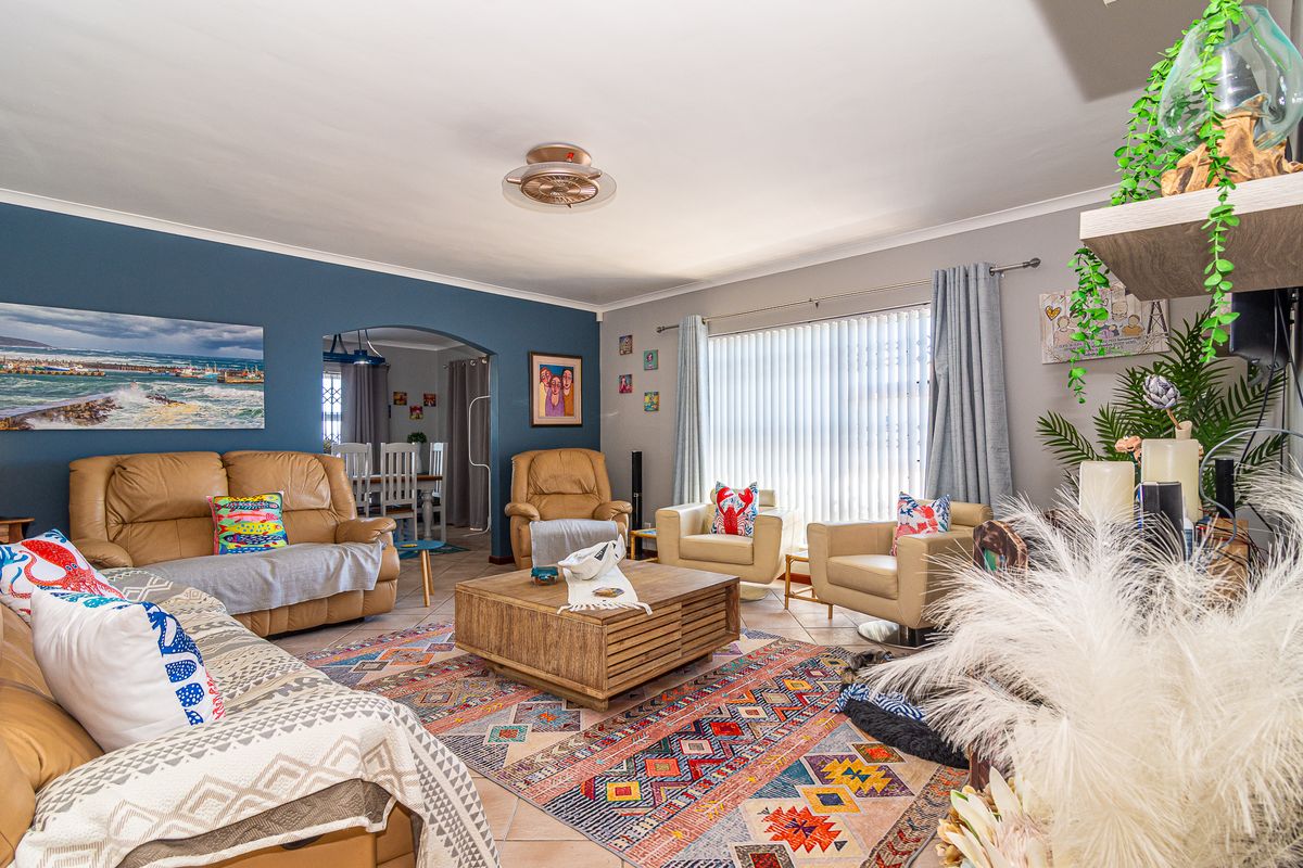 Spacious living room featuring tiled flooring, a ceiling fan, and an arched entryway leading to the dining area, with large windows and vertical blinds.