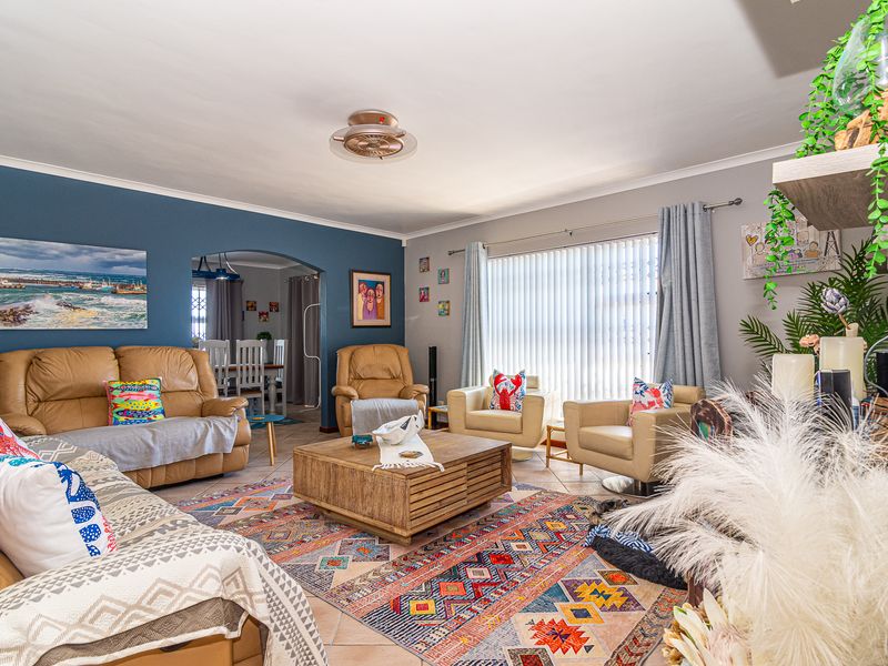 Spacious living room featuring tiled flooring, a ceiling fan, and an arched entryway leading to the dining area, with large windows and vertical blinds.