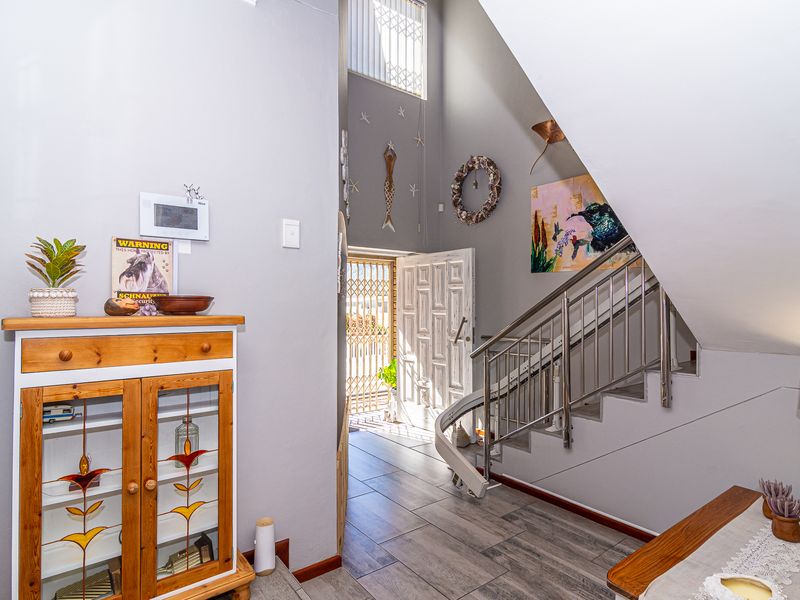 Welcoming entrance hall featuring a staircase with a stainless steel balustrade, a fitted stairlift, and modern tiled flooring leading to the main door.