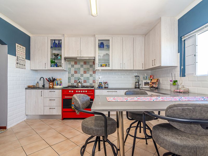 A well-maintained kitchen featuring light wood-grain cabinetry, a vibrant red gas stove, subway tile backsplash, and a functional integrated breakfast dining area.