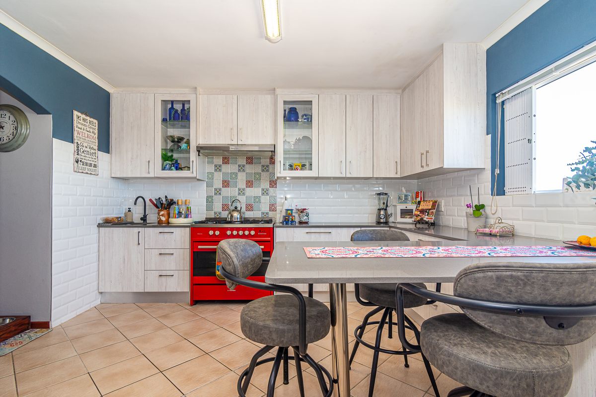 A well-maintained kitchen featuring light wood-grain cabinetry, a vibrant red gas stove, subway tile backsplash, and a functional integrated breakfast dining area.