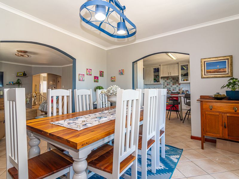 A bright dining room featuring tiled flooring and arched doorways leading to the kitchen and living areas, illuminated by a modern pendant light.