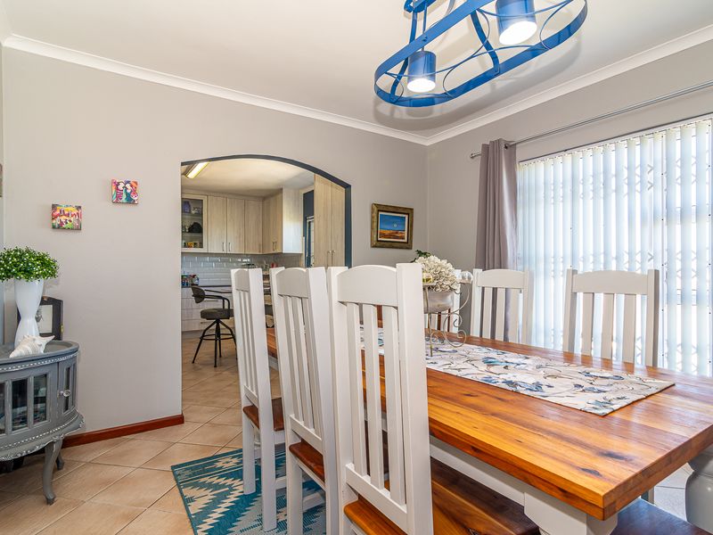 A bright dining room featuring tiled flooring, a decorative archway leading to the kitchen, and large windows with vertical blinds.