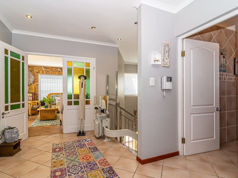 A bright, tiled hallway featuring a stairlift, recessed lighting, and elegant stained glass panel doors leading to adjacent living spaces.