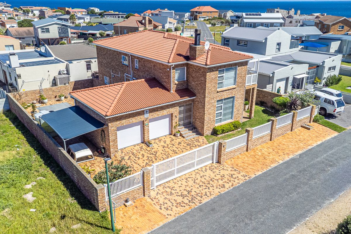 Aerial view of a double-story brick house featuring a paved driveway, double garage, carport, and secure perimeter walling in a coastal residential neighborhood.