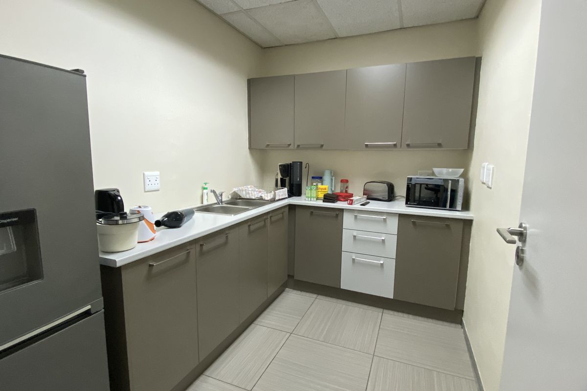 A functional office kitchenette featuring modern grey cabinetry, a stainless steel double sink, and tiled flooring.