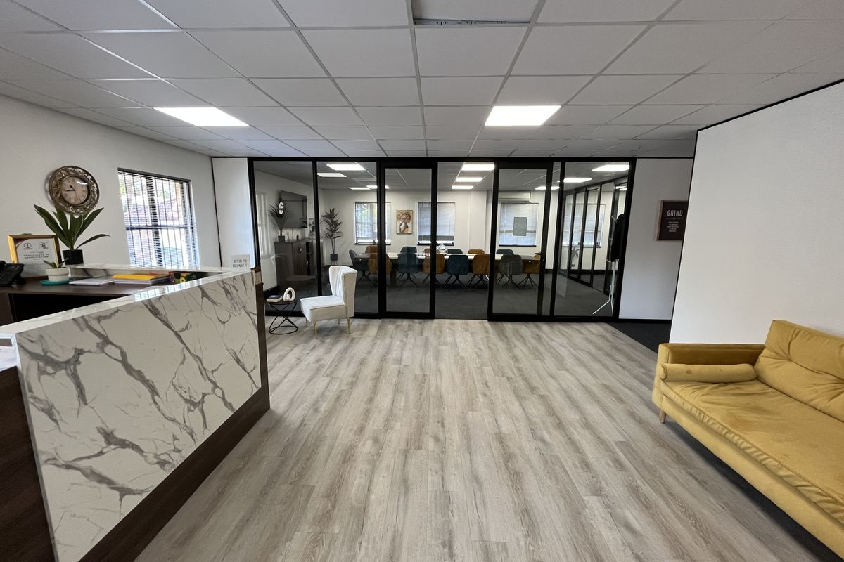 Modern office reception area featuring a marble-look desk, laminate flooring, and black-framed glass partitions leading to a conference room.