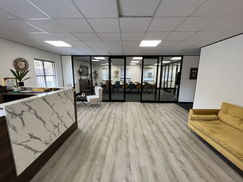 Modern office reception area featuring a marble-look desk, laminate flooring, and black-framed glass partitions leading to a conference room.