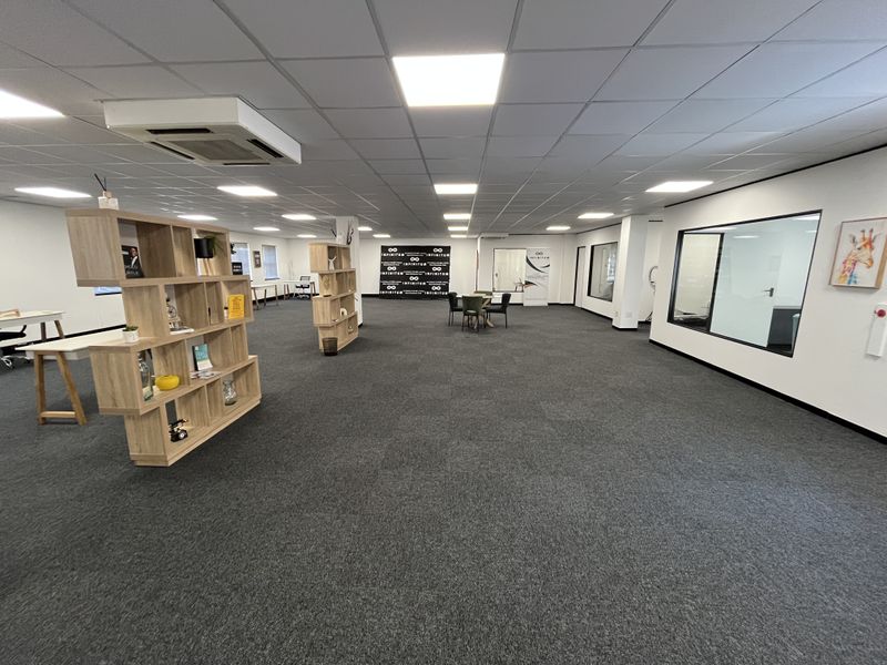Spacious open-plan office area featuring a suspended ceiling, recessed lighting, integrated air conditioning, and carpeted flooring with glass partition walls.