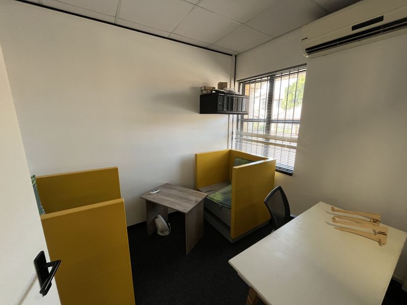 A functional office space featuring a suspended ceiling, wall-mounted air conditioning, and carpeted flooring, providing a practical environment for professional use.