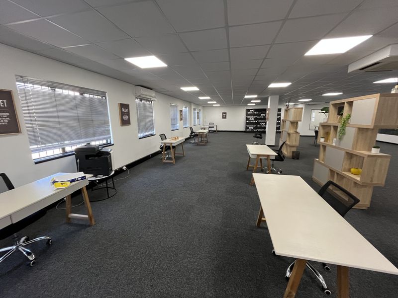 Spacious open-plan office area featuring suspended ceilings, recessed LED lighting, carpeted flooring, and multiple windows with venetian blinds.