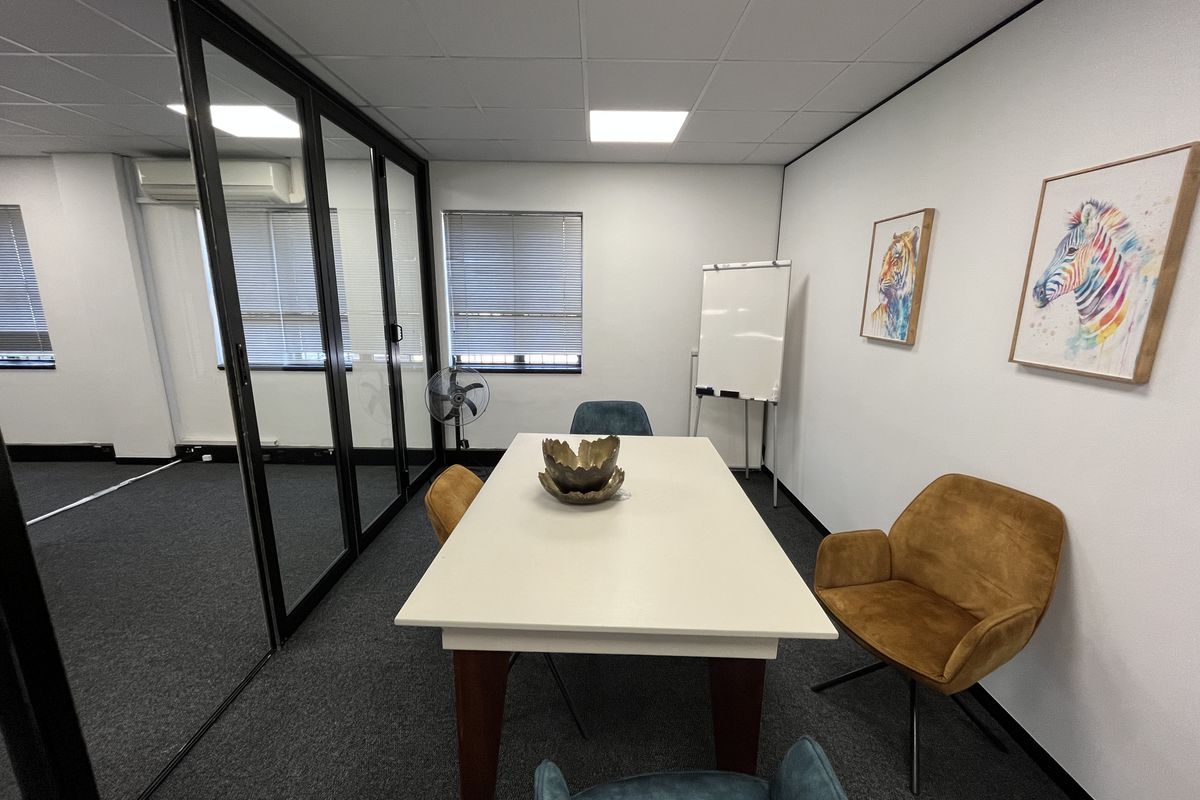 A modern office meeting room featuring a glass partition wall, suspended ceiling with recessed lighting, and carpeted flooring.