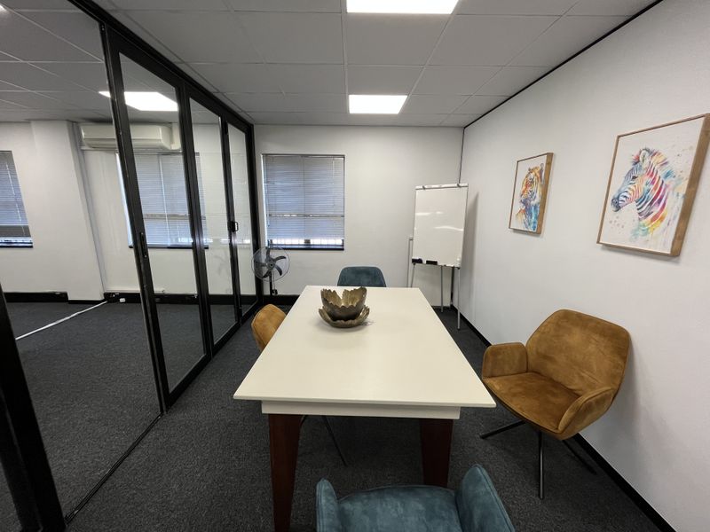 A modern office meeting room featuring a glass partition wall, suspended ceiling with recessed lighting, and carpeted flooring.