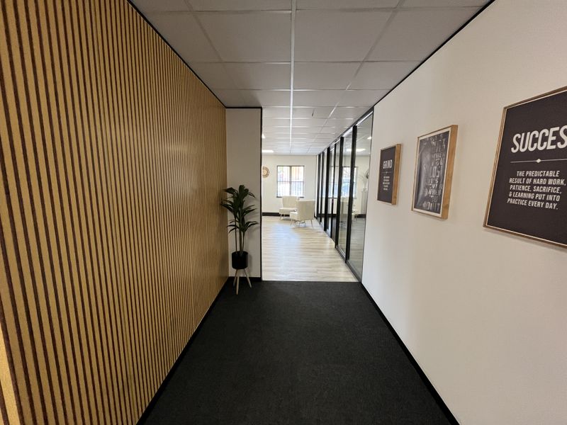 A modern office hallway featuring a striking slatted timber feature wall, glass partitions, and a combination of carpet and laminate flooring.
